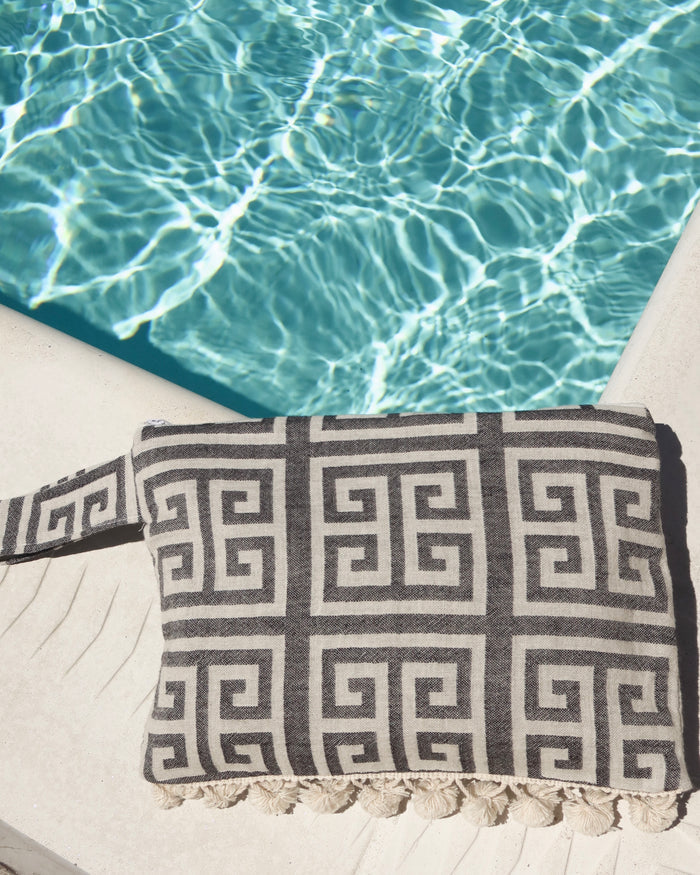 black and white greek key wet/dry zipper pouch clutch bag with cream pom pom trim next to a pool