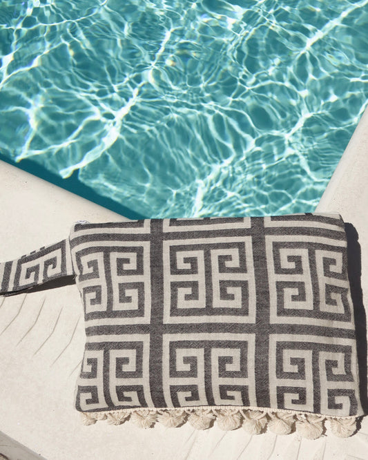 black and white greek key wet/dry zipper pouch clutch bag with cream pom pom trim next to a pool