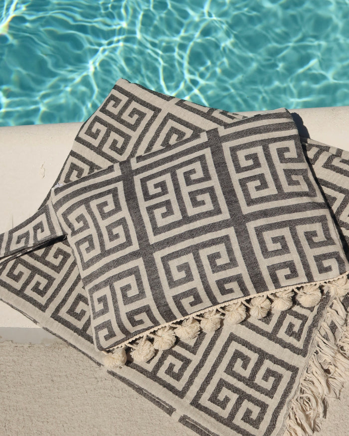 Black and cream/white greek key meander towel and matching clutch bag with pom pom trim and wet/dry water-resistant interior for the beach, made in Greece. Aelia Anna wet/dry bag at the pool