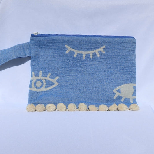 Blue clutch bag zippered wet/dry pouch with evil eye print and cream pom pom trim, made in Greece. Greek-inspired beach accessories