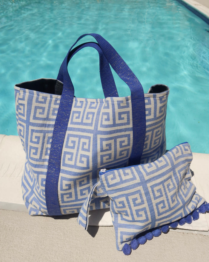 Blue and white greek key print beach bag and wet/dry clutch bag zippered pouch in front of a pool