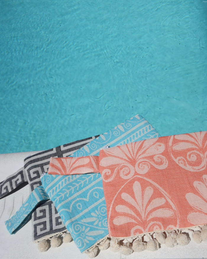 Colorful printed wet/dry clutch bags with pom pom trims by the pool. Water-resistant beach bags with zipper made in Greece, Greek brand Aelia Anna