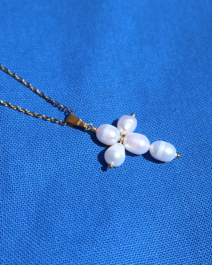 Freshwater earl cross necklace with a gold colored chain on a blue background made in Greece. Greek pearl cross necklace