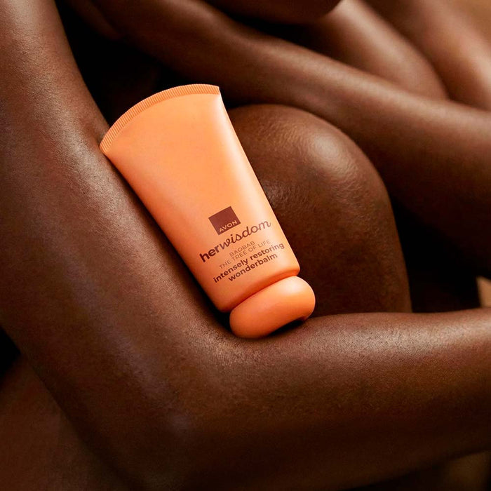 An orange tube of Her Wisdom Intensely Restoring Wonderbalm resting on smooth, dark brown skin.