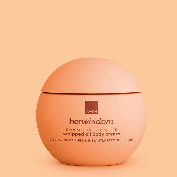 A round peach-colored jar of Avon Her Wisdom Baobab whipped oil body cream, set against a matching peach background.