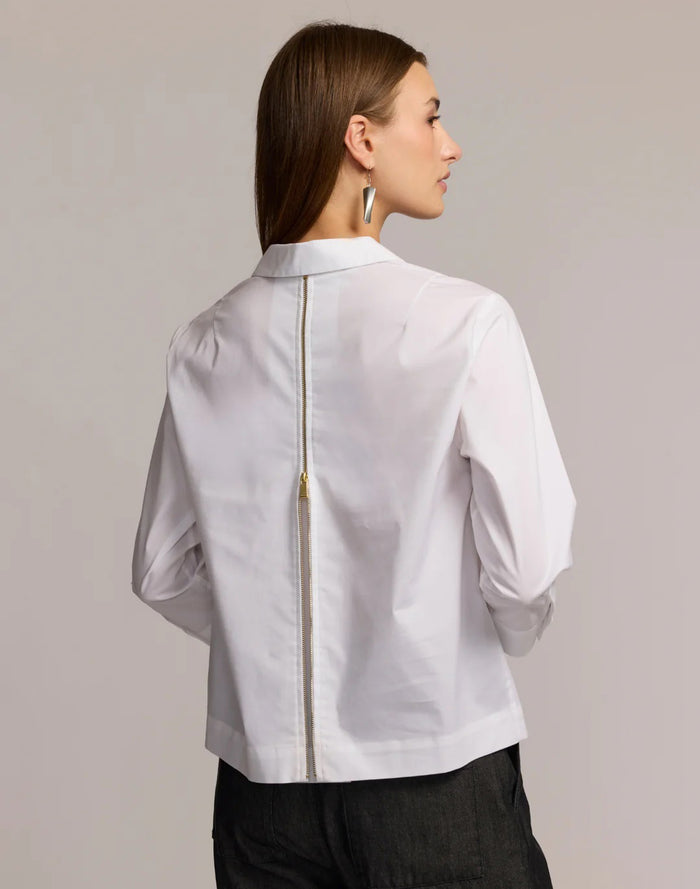 A woman stands against a plain, light background wearing the HINSON WU Alessa 3/4 Sleeve Shirt in stretch polished cotton—a crisp white blouse with a collared neckline and partial front zipper—paired with dark pants.