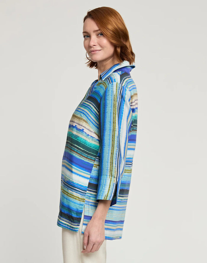 A woman wearing the HINSON WU VICKY 3/4 Sleeve Tencel Textured Stripe Print Top in blue, green, and white stripes with off-white pants stands smiling against a plain background, her light brown hair styled with hoop earrings.