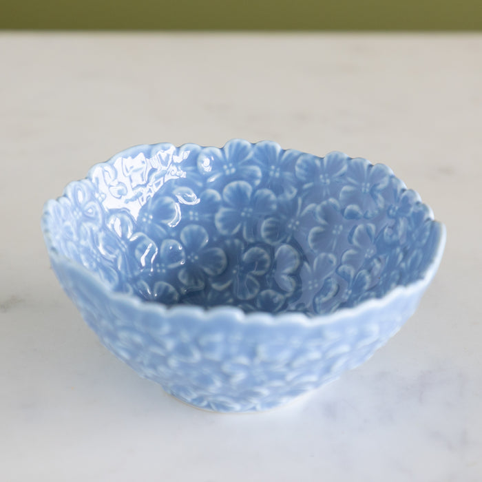 Blue ceramic bowl with hydrangea pattern on a white surface with a green background.