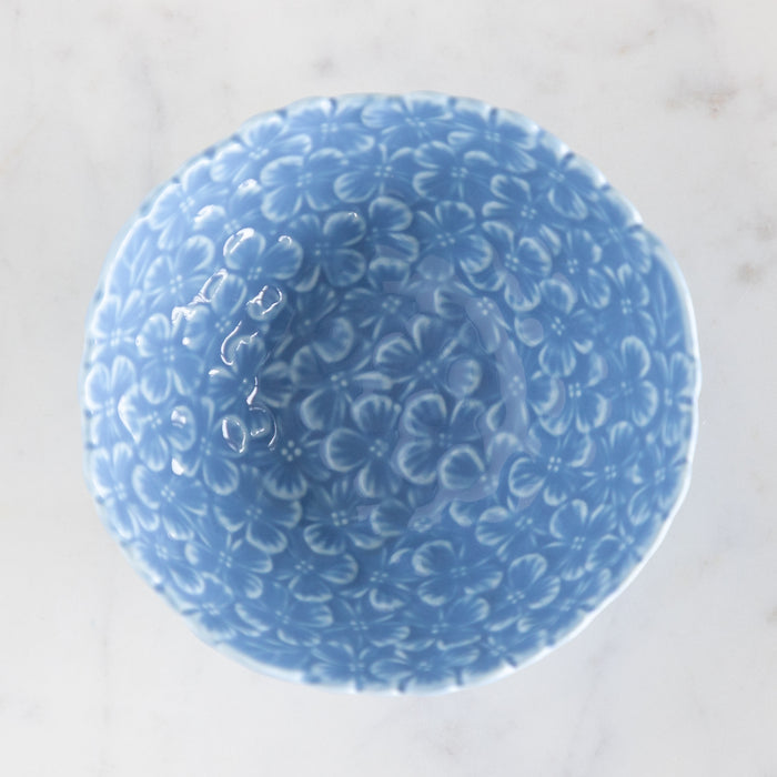 Blue ceramic bowl with hydrangea pattern on a white surface with a green background.