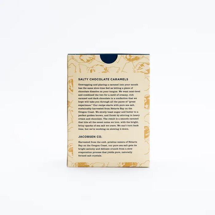 A rectangular box of JACOBSEN SALT CO. CHOCOLATE CARAMELS WITH SEA SALT stands on a light surface, featuring tan packaging with brown abstract patterns and a white label displaying the product name in black and gold.
