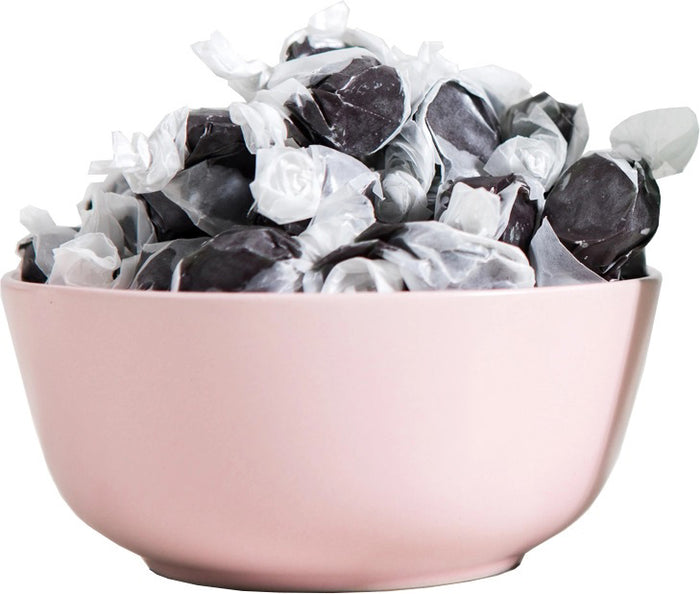 A dark blue JACOBSEN SALT - SALTY BLACK LICORICE BOX by JACOBSEN SALT CO. rests on a light surface against a plain gray background. Its white label with black text and abstract patterns hints at the sea salt and anise flavors inside.