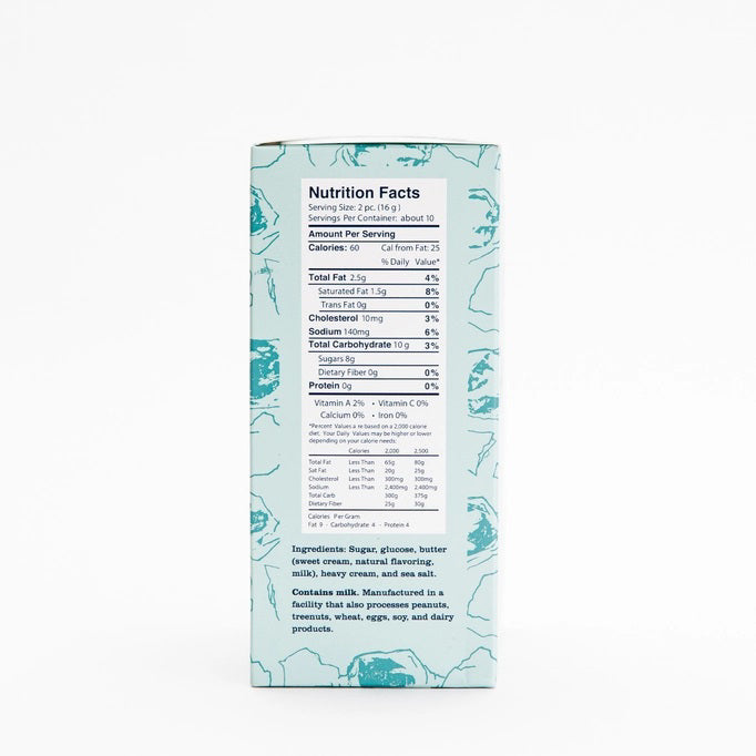 A light blue box of JACOBSEN SALT CO. JACOBSEN SALT - SALTY CARAMELS BOX, featuring a patterned design and product label on the front, rests on a light surface.