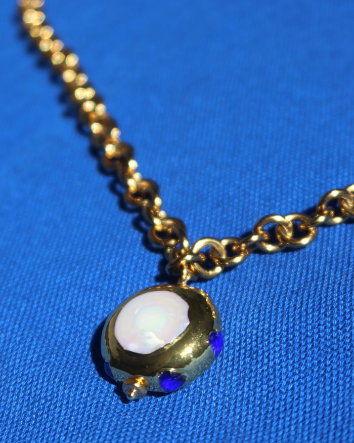 A gold chunky chain statement necklace with a jumbo freshwater pearl drop pendant with blue zircon stones surrounding it made in Greece. Greek jewelry