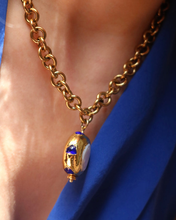 Woman wearing a gold chunky chain statement necklace with a jumbo freshwater pearl drop pendant with blue zircon stones surrounding it made in Greece. Greek jewelry