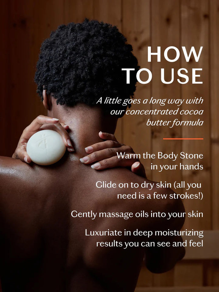 A round, off-white KATE MCLEOD Sleep Stone Deep Moisturizing Lotion Bar with calming lavender lies partly wrapped in a beige cloth inside an open green container. The wooden-lidded container rests on a smooth, light gray surface.