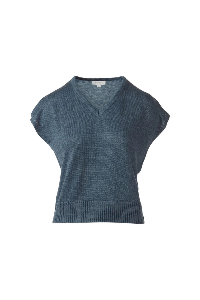 A woman in the KINROSS CASHMERE Cap Sleeve Vee Neck Linen Sweater with blue, brown, and tan stripes and white pants smiles softly against a plain white background.