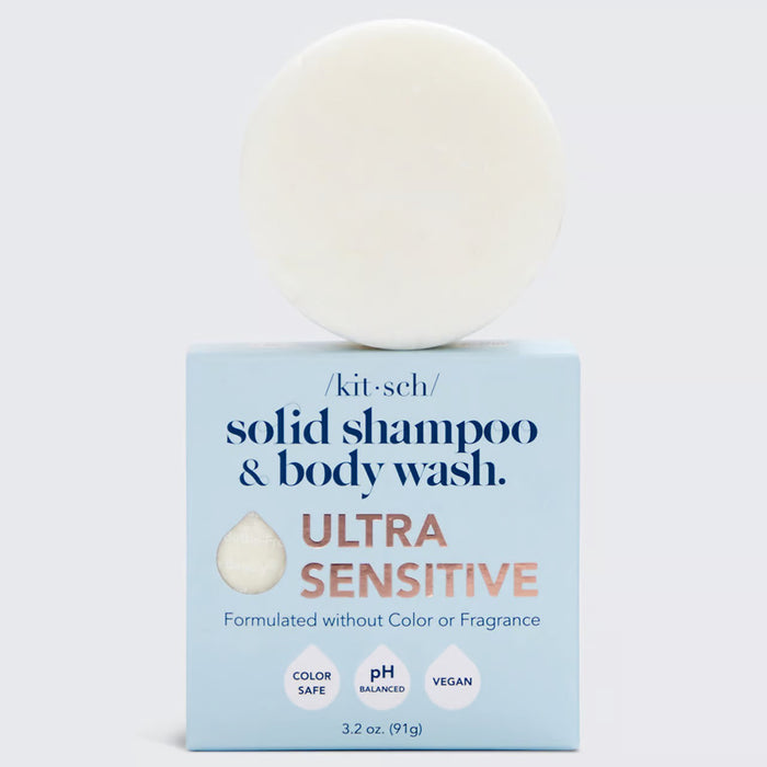 A round, cream-colored cleansing bar sits on a blue box labeled "KITSCH Ultra Sensitive Shampoo & Body Wash Bar." Packaging highlights include "4ocean Certified Cleanup Partner," "formulated without color or fragrance," "color safe," "pH balanced," and "vegan.