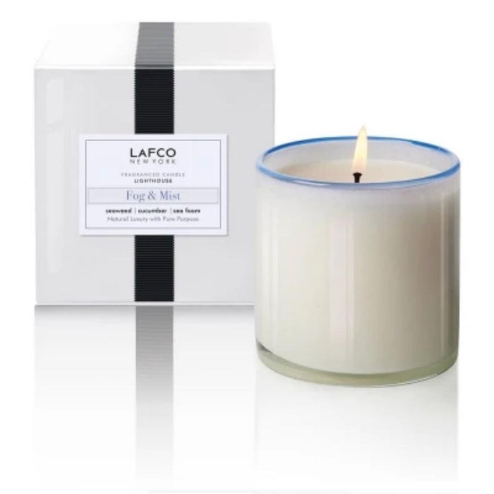 A lit LAFCO - FOG MIST, LIGHTHOUSE candle in a clear glass holder sits beside a white box with a black stripe and the LAFCO label.
