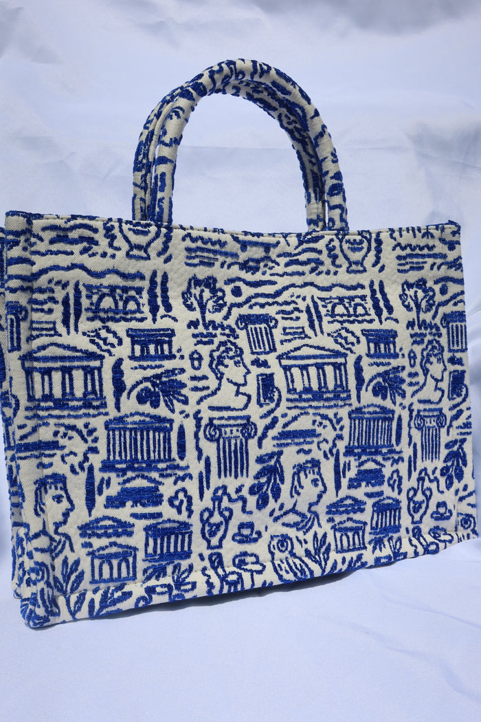 large cream/off-white handbag tote bag with a woven blue Greece print with the Parthenon, ancient Greek sculptures, owls, ionian columns, olive branches, olive trees, and more. Handcrafted bag made in Greece