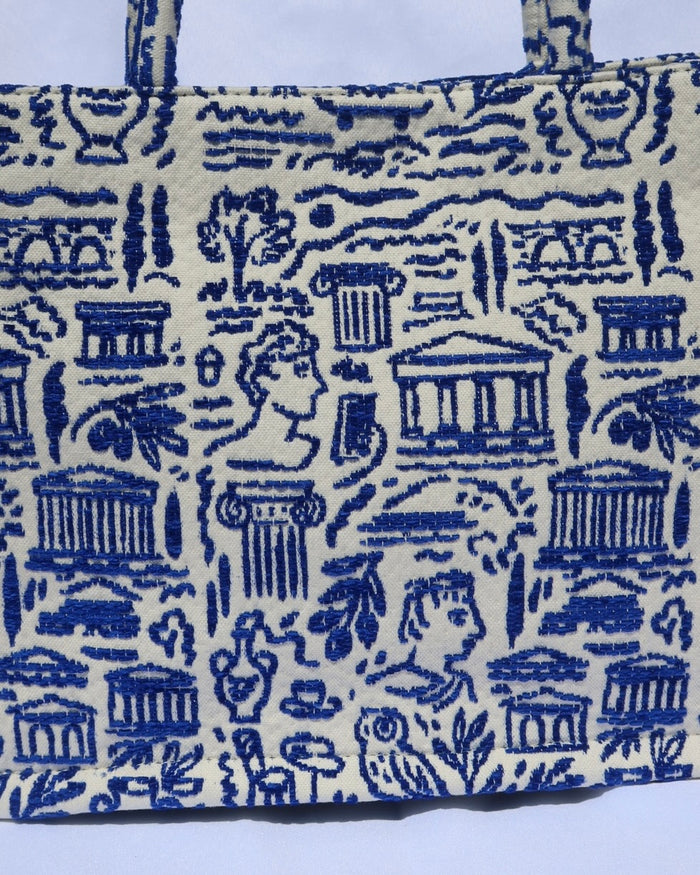 large cream/off-white handbag tote bag with a woven blue Greece print with the Parthenon, ancient Greek sculptures, owls, ionian columns, olive branches, olive trees, and more. Handcrafted bag made in Greece
