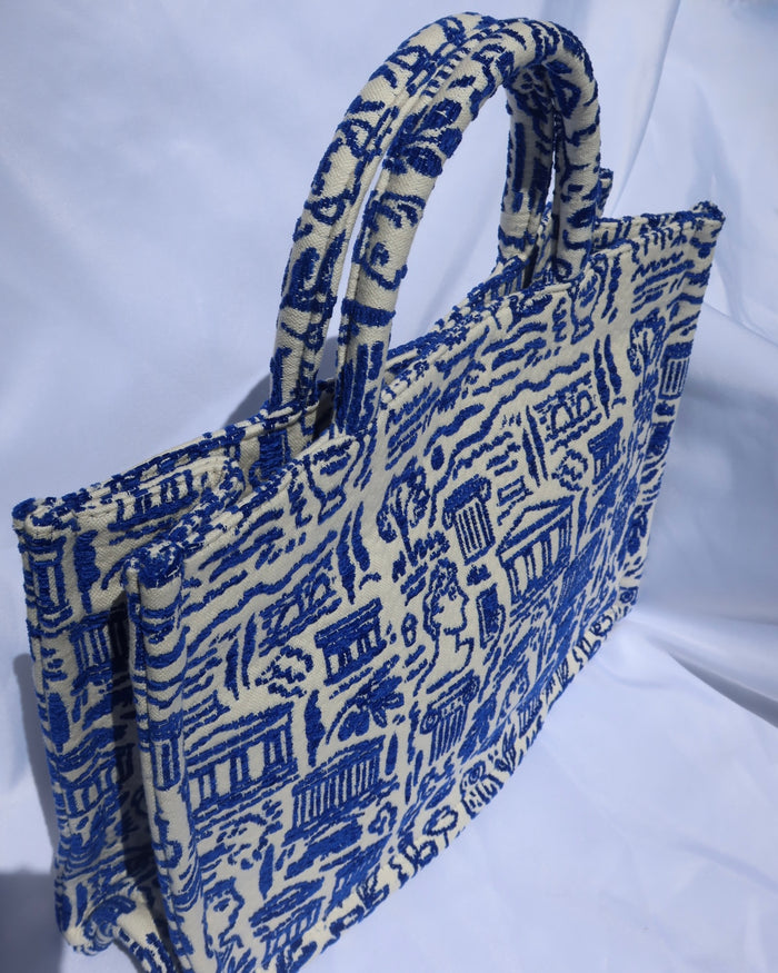 large cream/off-white handbag tote bag with a woven blue Greece print with the Parthenon, ancient Greek sculptures, owls, ionian columns, olive branches, olive trees, and more. Handcrafted bag made in Greece