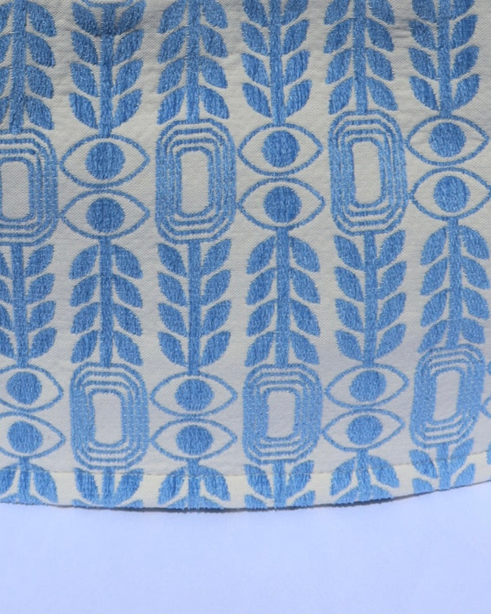 Light blue woven print with olive branches, evil eyes, and abstract geometic shapes
