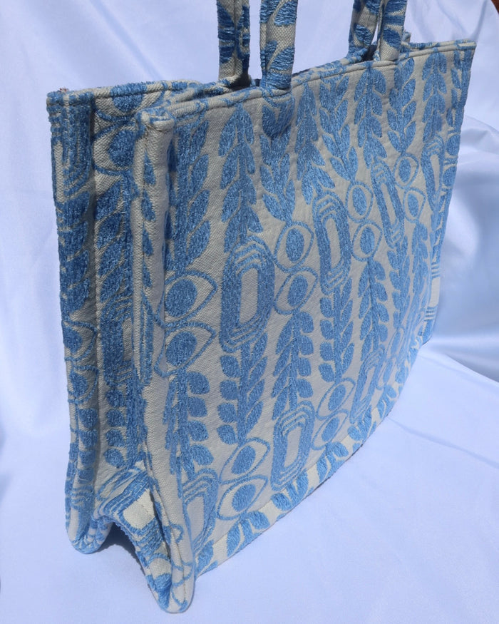 large handbag with woven light blue motif featuring evil eyes, olive branches, and abstract shapes handcrafted in Greece. Greek artisinal handbag