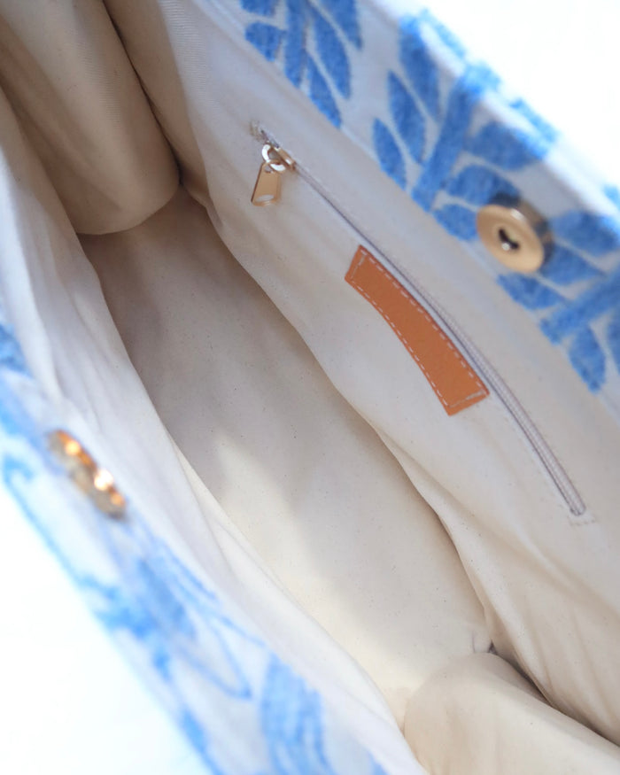interior of large handbag with woven light blue motif featuring evil eyes, olive branches, and abstract shapes handcrafted in Greece. Greek artisinal handbag