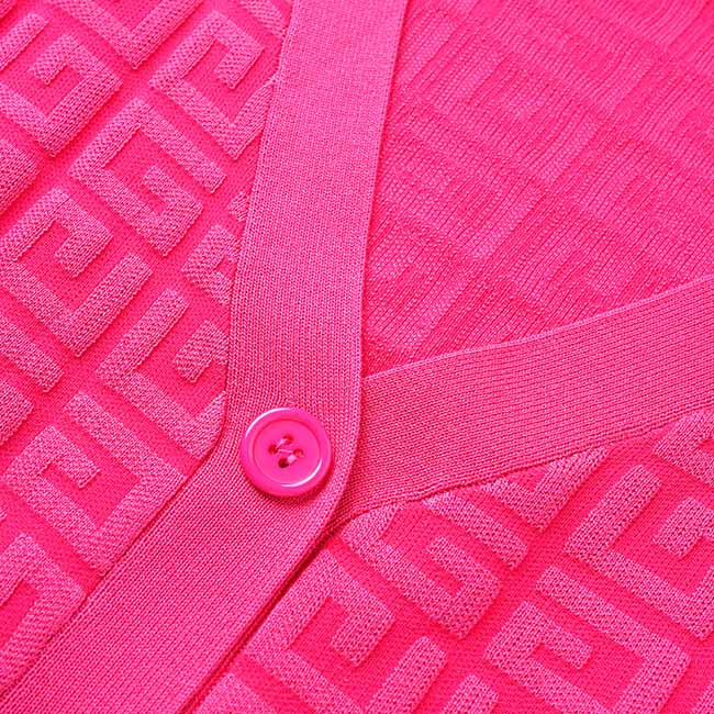 Close-up of a vibrant pink button detail on a long knitted cardigan set with a textured pattern