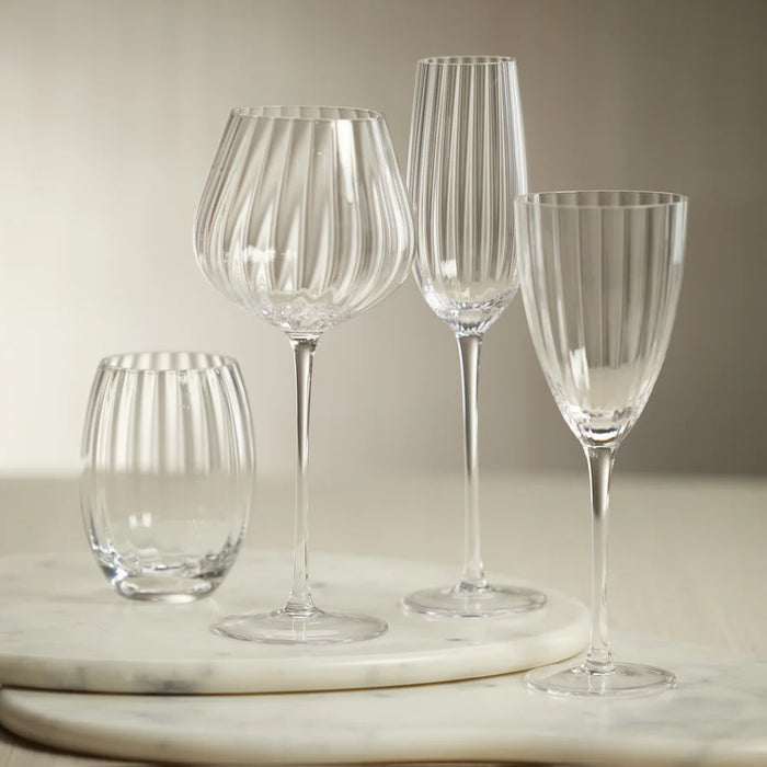 The ZODAX MADELEINE OPTIC CHAMPAGNE FLUTE, with vertical ridges and a long stem, stands upright on a white background—perfect for serving alongside a 270 ml water bottle or 9.13 oz bottle.