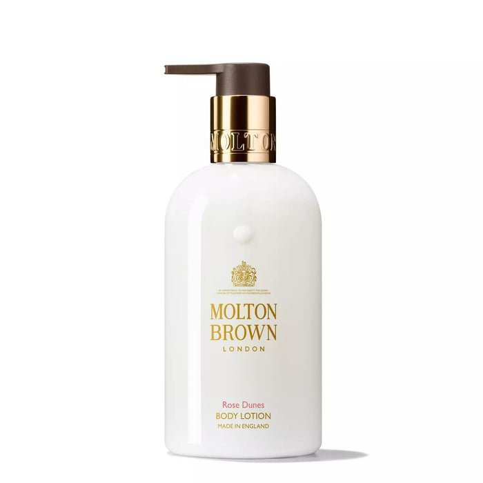 A white bottle of MOLTON BROWN Rose Dunes Body Lotion with a gold pump and label, shown on a plain white background. This moisturising lotion hydrates skin with a luxurious ambery-rose fragrance.
