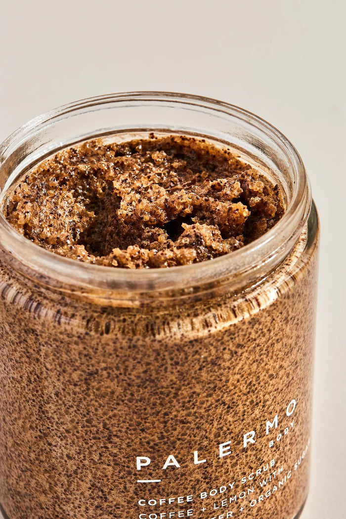 A clear jar with a black lid holds PALERMO BODY’s COFFEE & LEMON BODY SCRUB, an exfoliating sugar scrub with shea butter and organic sugar (8.5oz/240g). The brown, granular formula is a favorite for cellulite treatment.