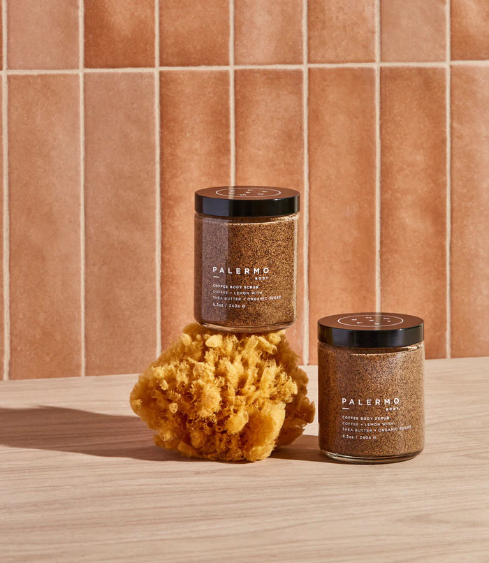 A clear jar with a black lid holds PALERMO BODY’s COFFEE & LEMON BODY SCRUB, an exfoliating sugar scrub with shea butter and organic sugar (8.5oz/240g). The brown, granular formula is a favorite for cellulite treatment.