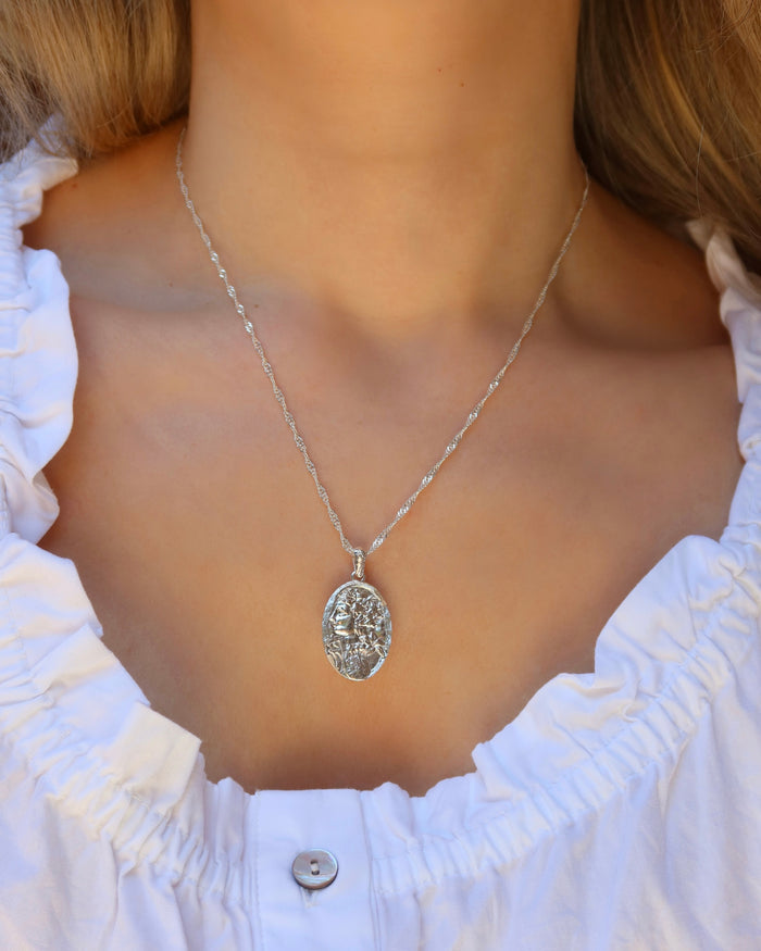 Woman wearing a silver oval pendant necklace of the Greek goddess Persephone, goddess of the spring and queen of the Underworld on a sterling silver 925 singapore twisted chain made in Greece. Greek mythology jewelry
