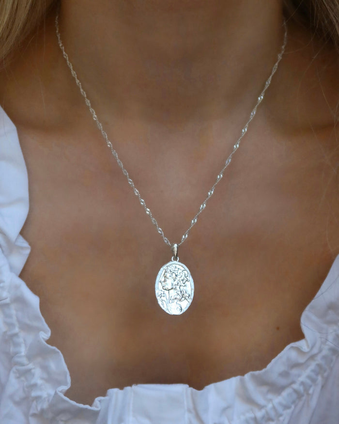 Woman wearing a silver oval pendant necklace of the Greek goddess Persephone, goddess of the spring and queen of the Underworld on a sterling silver 925 singapore twisted chain made in Greece. Greek mythology jewelry