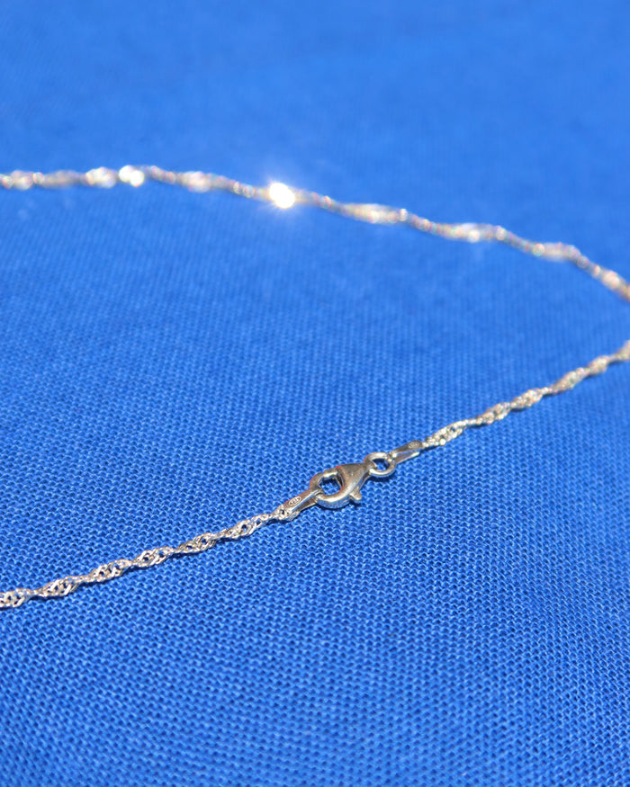 Silver twisted Singapore chain necklace with lobster claw clasp on a blue fabric background