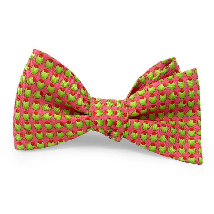 The PETER-BLAIR Olives Silk Bow Tie in Coral by BIRD DOG BAY features a playful olive pattern on coral 100% silk and includes an adjustable neck for a perfect fit.