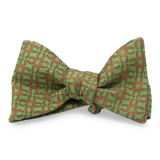 The BIRD DOG BAY PETER-BLAIR RINGERS Silk Bow Tie in green features a handmade design with small red horseshoes, an adjustable neck, and is displayed neatly tied against a white background.