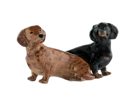 The QUAIL CERAMICS - DACHSHUND SALT AND PEPPER SET by QUAIL DESIGNS features hand painted brown and black dachshund stoneware figurines. Both decorative and dishwasher safe, they sit together on a white background.