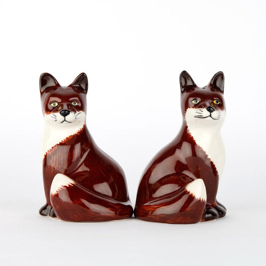 The QUAIL DESIGNS QUAIL CERAMICS - FOX SALT AND PEPPER SET features two handpainted stoneware shakers with reddish-brown and white fur, upright ears, bushy tails, and alert expressions, shown side by side on a white background.