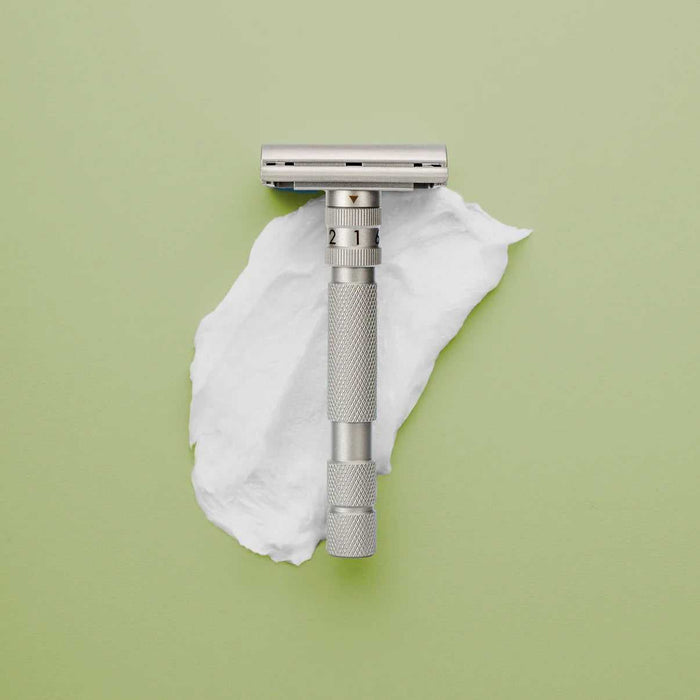 Stainless steel safety razor with adjustable settings on a green background