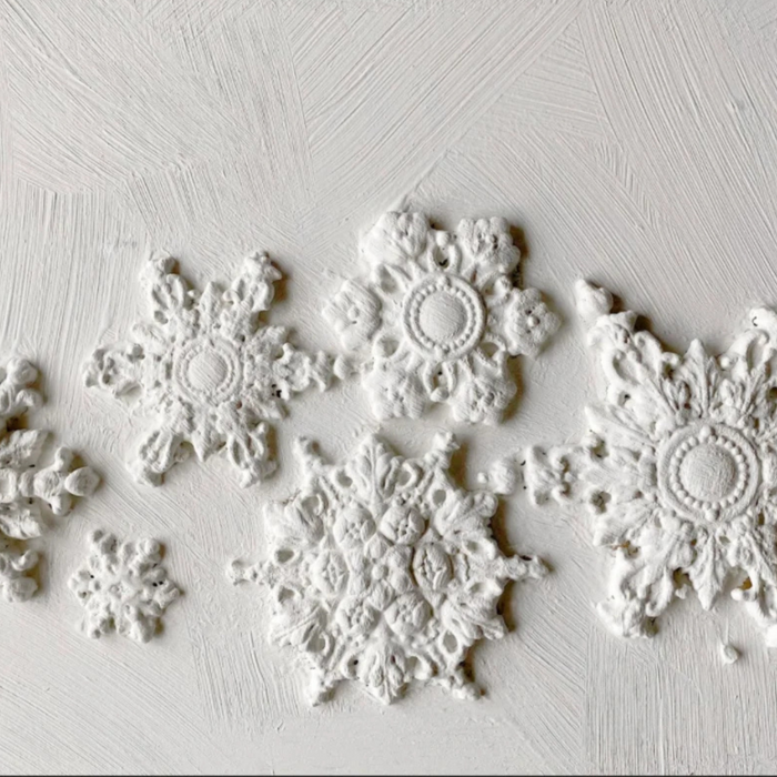 White embossed snowflake wall decals arranged on a textured white plaster background.