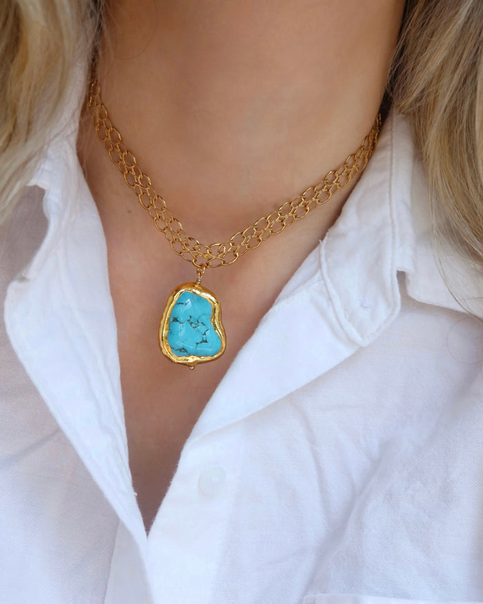 Woman wearing a gold chain necklace with a large turquoise pendant made in Greece, Greek jewelry statement necklace