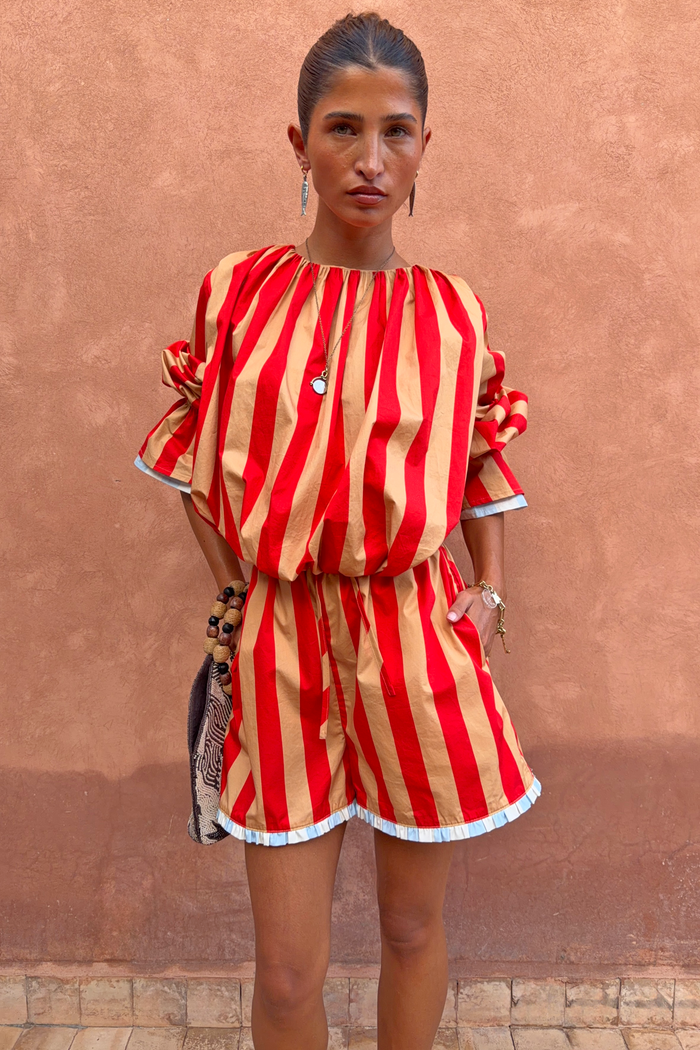 Tomato Stripe Ellie Shorts in red and camel cotton co-ord with contrast hem trim against a textured wall.