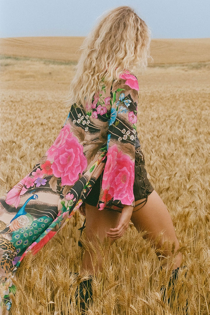 Back view of a model wearing Valley of the Dolls Duster, wide sleeves catching wind in a wheat field