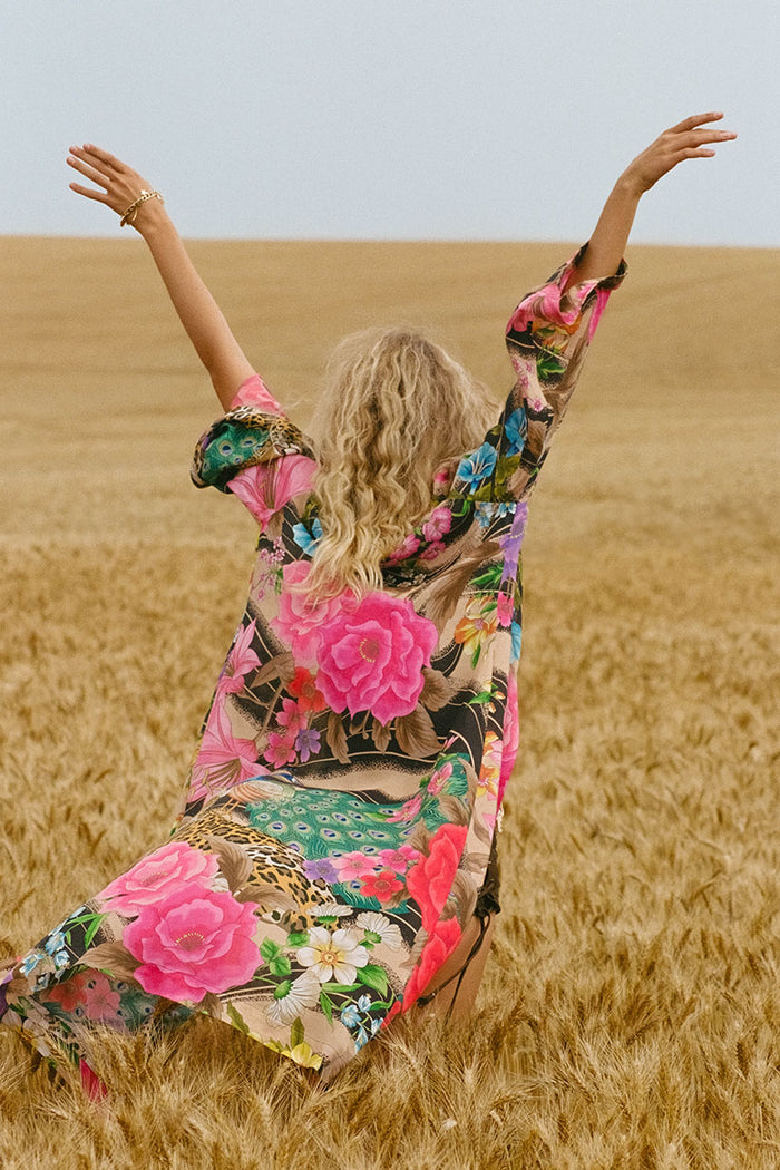 Back view of a model wearing Valley of the Dolls Duster, arms raised in wheat field, floral ECOVERO viscose