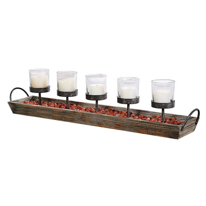 The CREATIVE COOP VOTIVE HOLDER features a rectangular wood and metal frame with handles, five white candles in glass votives on black stands, and decorative pebbles at the base—ideal for creating cozy fireplace ambience.
