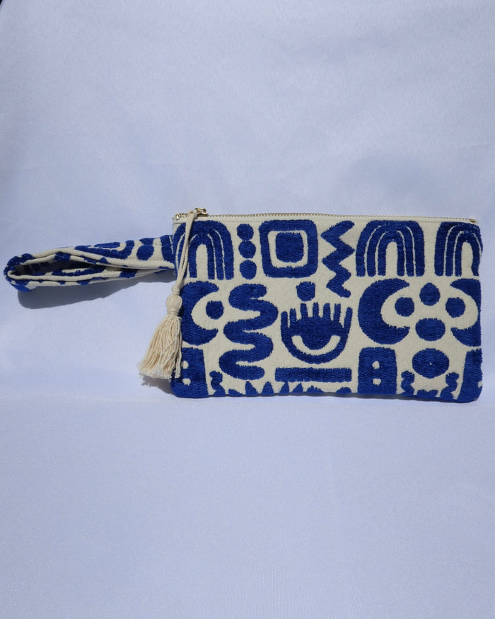 Wristlet clutch bag with a cream background and woven blue geometric symbols design with an evil eye, rainbow, moons, etc.
