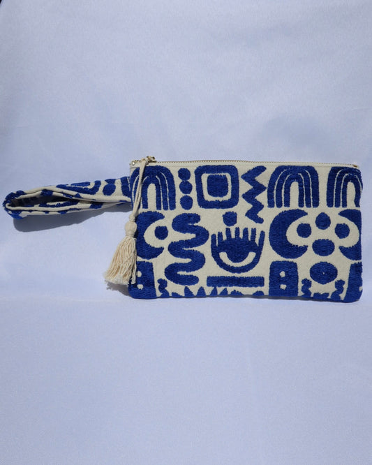 Wristlet clutch bag with a cream background and woven blue geometric symbols design with an evil eye, rainbow, moons, etc.