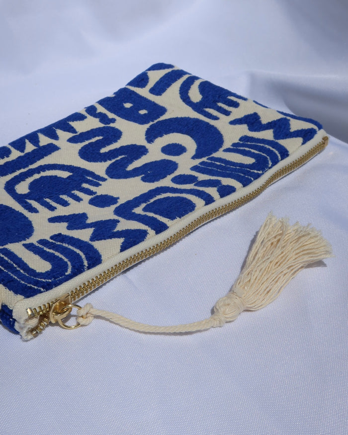 Wristlet clutch bag with a cream background and woven blue geometric symbols design with an evil eye, rainbow, moons, etc. with a gold zipper and tassel